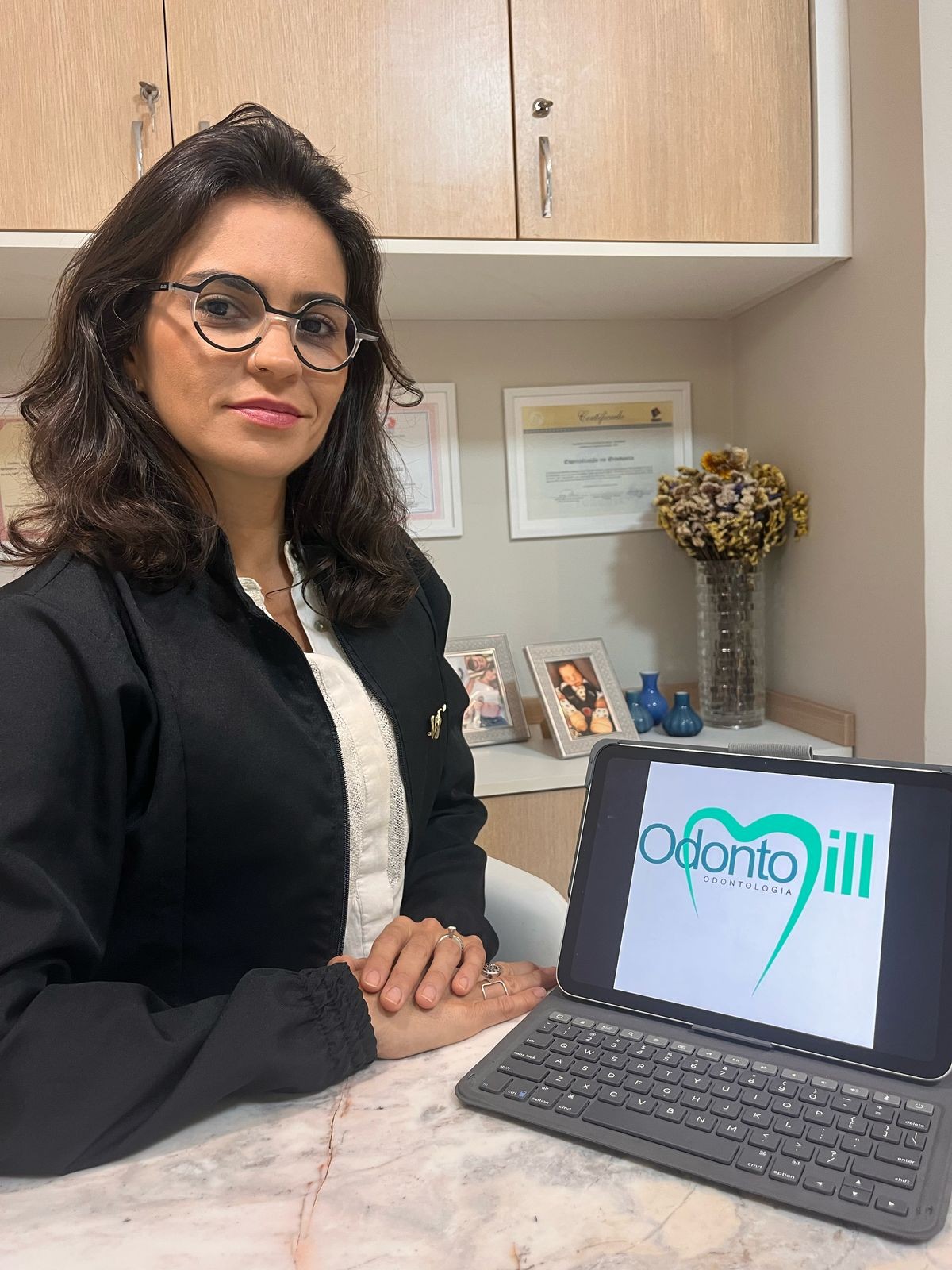Dentista da Odontomill sentada no consultório, com o logotipo da clínica no tablet